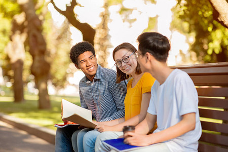 学生活方式三个千禧一代谈论课程放松坐在户外的长凳上图片