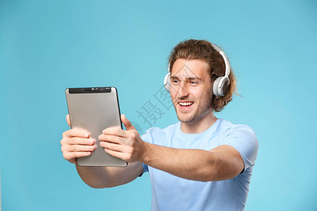 英俊的男人带着平板电脑和彩色背景的耳机图片