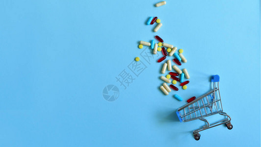 蓝色背景上装有各种药丸的购物手推车药店网上药店制药公司经营理念的创意平面布局选择焦图片