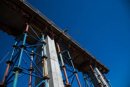 建设跨河公路桥交汇处建筑工地上的建筑工人和建筑设备对蓝天背景图片