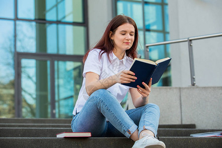 校园里户外的大学生坐在楼梯上拿着书一个自信的学生拿着书在大学建设图片