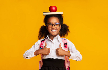 快乐的黑人女孩持有书和苹果在黄背景上游览时的头部闪烁缩略图图片