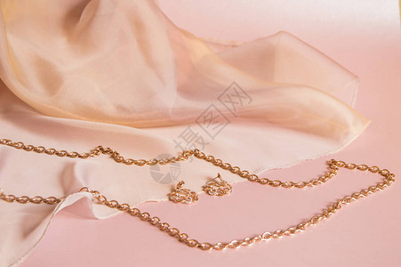 金链和耳环贴在粉色丝绸背景上图片