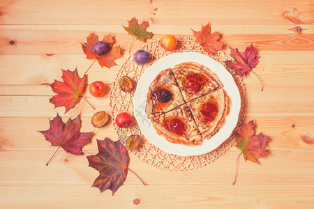 白色盘子上有自制李子果酱的煎饼新鲜李子和木本底的秋叶托恩图图片