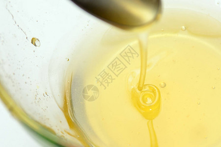 液体蜂蜜从茶匙里倒到透明杯子里概念图片