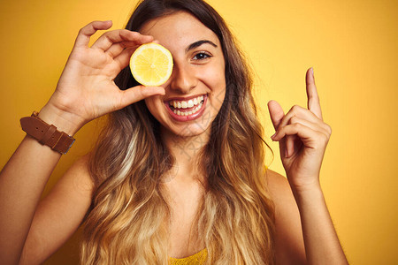 年轻美女在黄色的孤立背景上拿着柠檬对着眼睛以手和指向另一图片