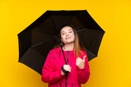 黑发小女孩在孤立的黄色背景上举起雨伞图片