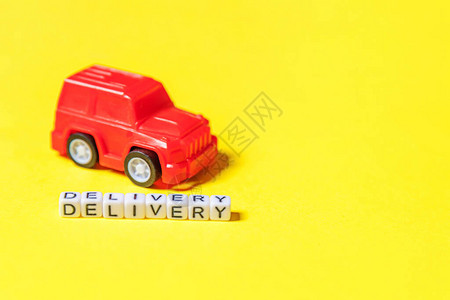 只需设计红色玩具车和在黄色彩背景上隔离的题词DELIVERY字网上购物网上购买电子商务包裹送货服务概背景图片