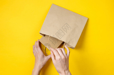 女手在黄色背景的纸袋里放一个纸箱图片