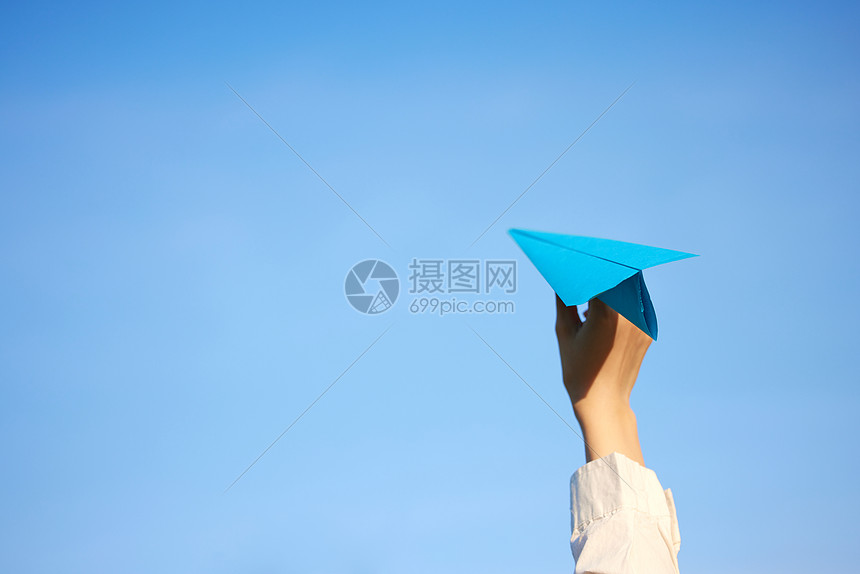 蓝天背景手举纸飞机的手部特写图片