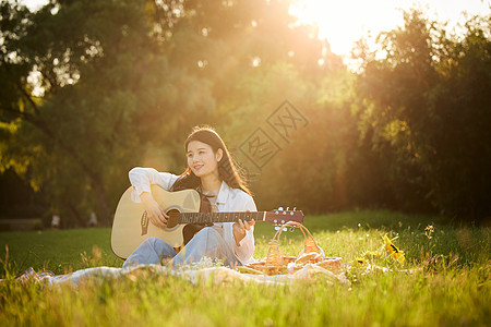 秋天弹吉他女生阳光下的青年美女坐在草地上弹吉他背景