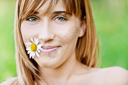 美丽的年轻成年人将鲜花放在嘴里与绿色的背景图片