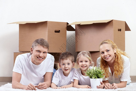 在纸板盒背景下有孩子的家庭在地毯上以纸图片
