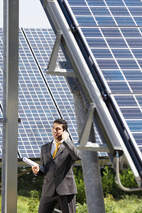 成人中意大利男工程师在太阳能发电站持有蓝图并在移动电话上交谈的肖像图片