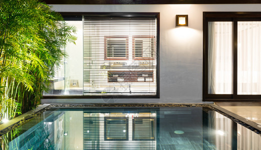 酒店套房内设有游泳池背景中通往浴室的门带窗帘和百叶窗的户大游泳池附近的棕图片