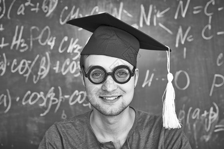 黑板背景上戴着毕业帽和眼镜看着相机的英俊学生的黑白图像背景