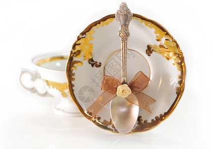 银色茶匙与金色背景杯碟上的蝴蝶结图片