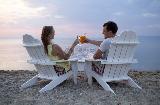 坐在沙滩上木制甲板椅子上的一对浪漫夫妇在的夕阳下举杯合在一图片
