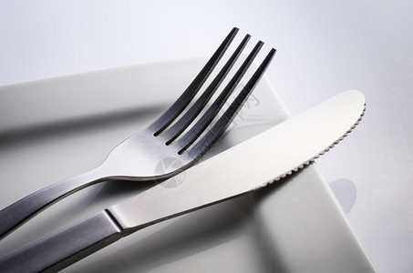 用叉子刀在白盘上的用过的餐具在灰色的图片