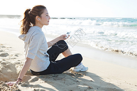 一位年轻女子坐在细沙海滩岸边的侧面肖像视图图片