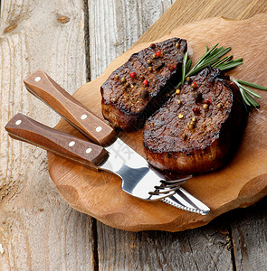 烤牛排配香料和迷迭香在木板上用叉子和餐桌刀在质图片