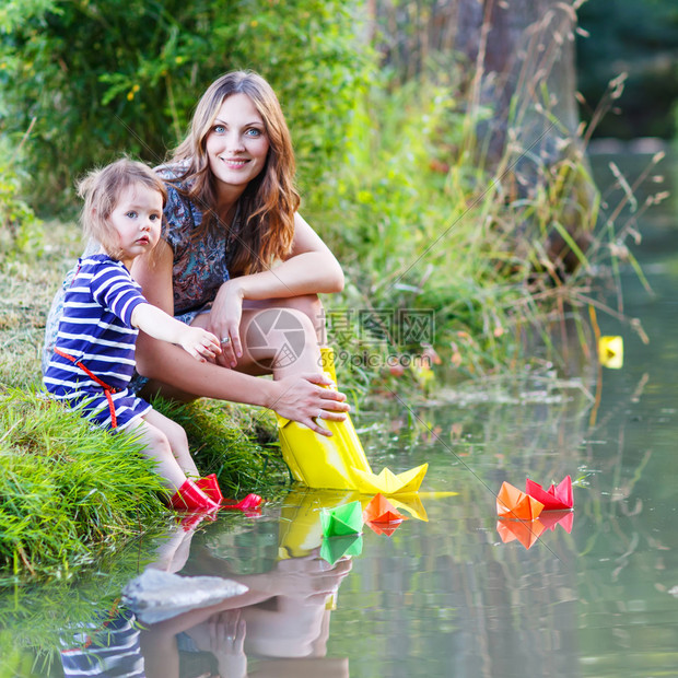 年轻漂亮的女人和她的小女儿在河里玩纸船与孩子图片