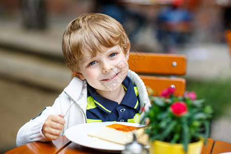 可爱的金发小男孩夏天在德国一个老城中心的外边咖啡厅里笑着吃蛋糕在温暖图片