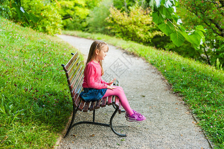 可爱的小女孩在公园玩耍坐在长椅上在阳光明媚的图片