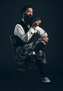 留着胡子的苏格兰人在黑暗中坐在他的苏格兰短裙的椅子上享受睡帽图片