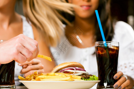 两名妇女一名是非裔美国人在快餐厅吃汉堡包和苏打汽背景图片