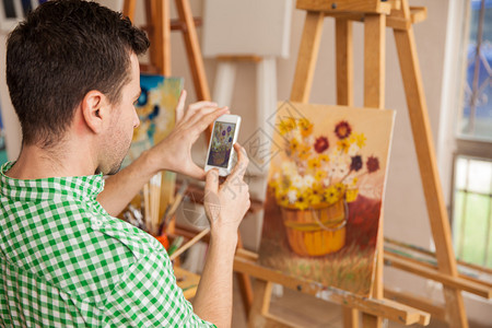 年轻男艺术家用智能手机拍摄他的艺术作品照片图片