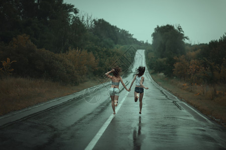 年轻女孩在雨中在路上奔跑图片