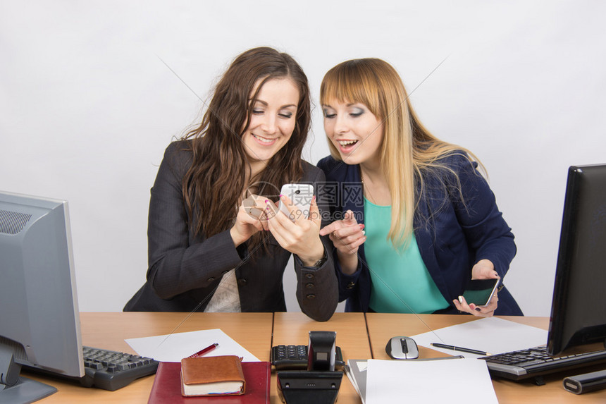 两名年轻办公室雇员在办公桌用手机处理私人事务图片