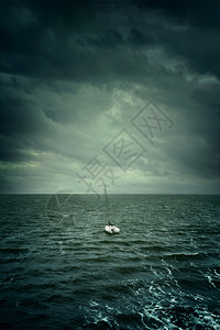 一艘小帆船漂浮在动荡的水域和暴风背景图片