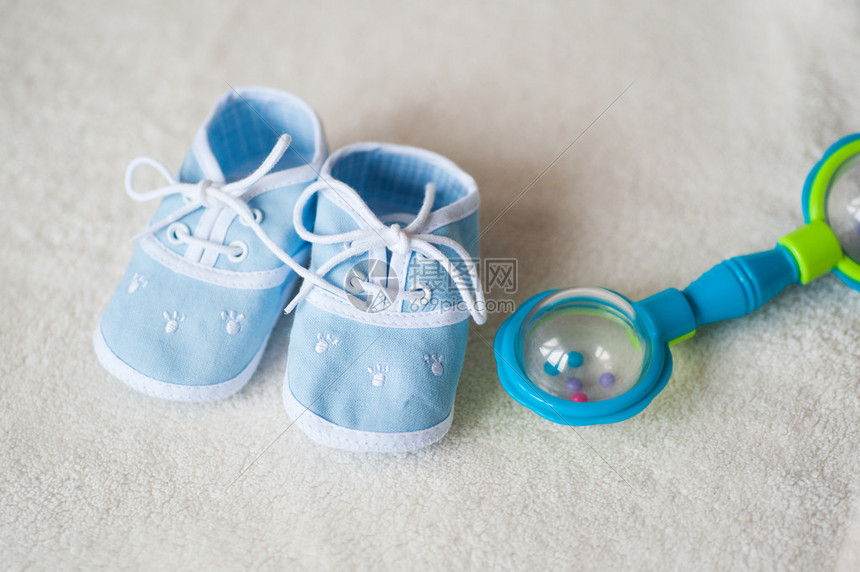 浅色背景中的蓝色婴儿鞋和拨浪鼓图片