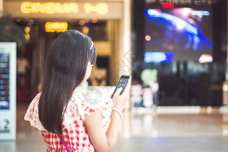 快乐的亚洲女孩正在利用智能手机在购物中心进行前门图片