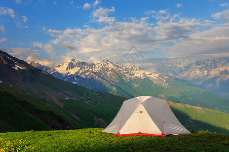 高草地上的灰色帐篷在山脉和岩石背图片