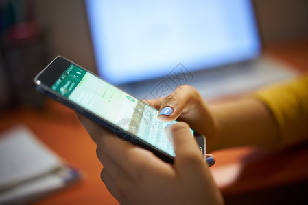 年轻女使用手机在夜间社交网络上发送短信用电脑笔记本电脑亲近手接背景图片