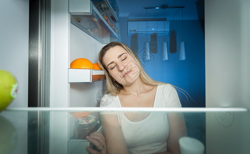 穿着睡衣的疲惫女人在深夜看着冰箱里的肖像图片