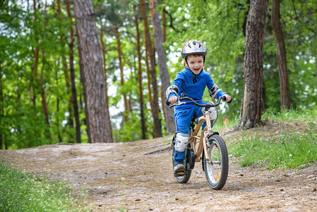 男生睡觉穿着五颜六色的雨衣的快乐有趣的小男孩在寒冷的森林里骑着他的第一辆自行车户外儿童的积极休闲快乐无忧背景