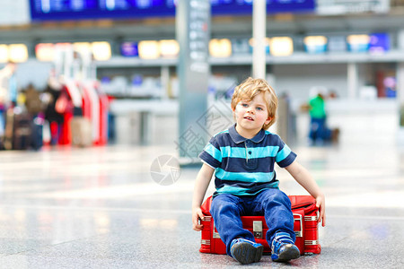 可爱的小男孩坐在机场的手提箱上图片