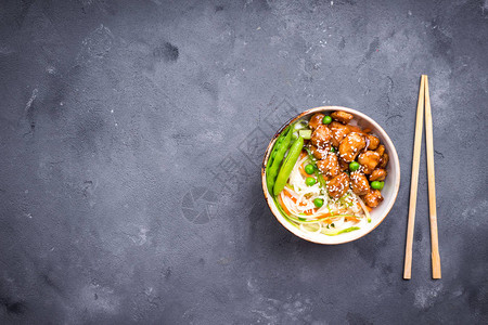 亚洲风味面条配照烧鸡肉蔬菜和青豆荚在质朴的混凝土背景上的碗里的面条中式泰式日式炒面文本的背景图片