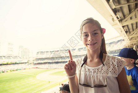 一个微笑的快乐小女孩在观看职业棒球比赛时显示出1号手指标志她正在享受在一个大球场观看她最喜欢图片
