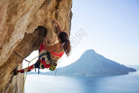 年轻女在悬崖上挣扎着攀登顶峰与海图片