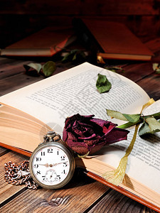 一朵红玫瑰在一本被时间泛黄的旧书和一张旧木桌上的古董怀表的图片