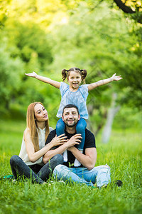 年轻快乐的三口之家在户外玩得开心漂亮的小女儿在她父亲的背上父母和女孩看起来很高兴和微笑家庭生活中的幸福与和谐外图片
