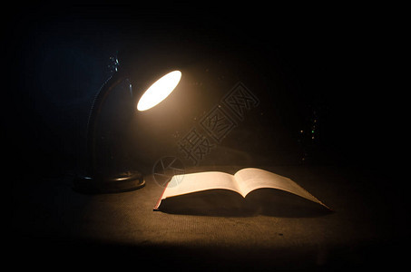 在黑暗背景的发光桌灯旁打开书背景图片