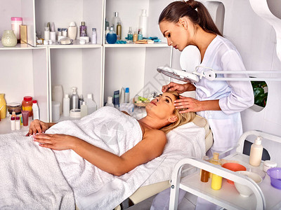 水疗沙龙中年妇女的眉毛治疗美容师用镊子夹眉毛40多岁的女在化妆灯下欧洲面部程序去除皱纹图片