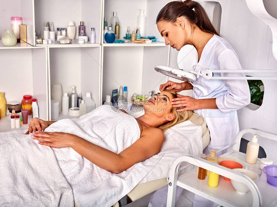 水疗沙龙中年妇女的眉毛治疗美容师用镊子夹眉毛40多岁的女在化妆灯下欧洲面部程序去除皱纹图片
