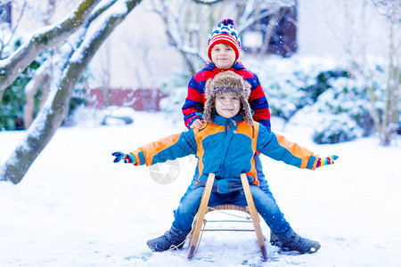 两个男孩在降雪期间享受乘坐雪橇孩子们在雪地上拉雪橇兄弟姐妹骑着雪橇双胞胎在户外玩耍朋友们在白雪皑的冬季公园拉雪橇家庭圣诞假图片